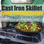Chicken recipe cast iron skillet by CampingForFoodies features a large cast iron skillet sitting on a propane camp stove. The pot is filled with a dinner that is ready to be served. The chicken is cooked with black beans and corn and is topped with fresh avocado and cilantro with text over the image that reads cast iron skillet camp chicken recipe, camp stove, RV stove, and campfire.