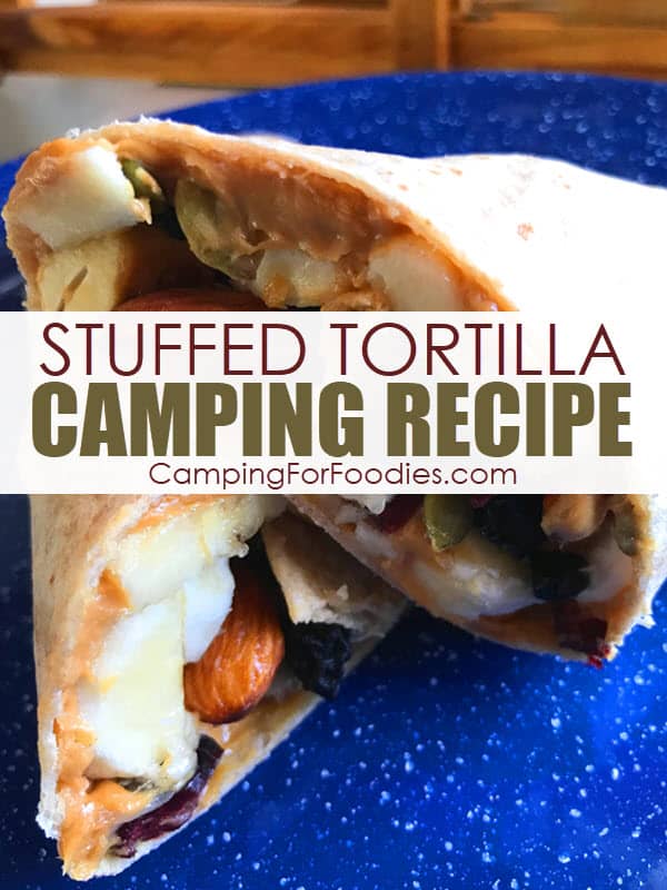 Fruit And Nut Peanut Butter Stuffed Tortilla by CampingForFoodies features a whole wheat tortilla stuffed with peanut butter, banana slices, dried fruit, nuts and seeds all rolled up and ready to serve on a blue camping plate with text over the image reading stuffed tortilla camping recipe.
