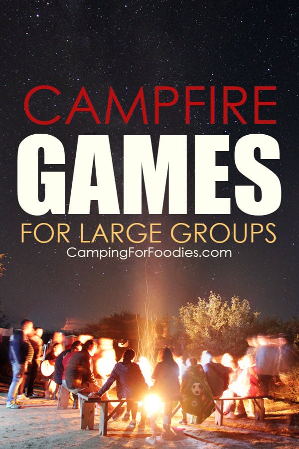 Games for camping large groups to play around a campfire by CampingForFoodies features a dark night sky filled with stars and a bright campfire surrounded by a big group of campers and text over the image that reads campfire games for large groups.