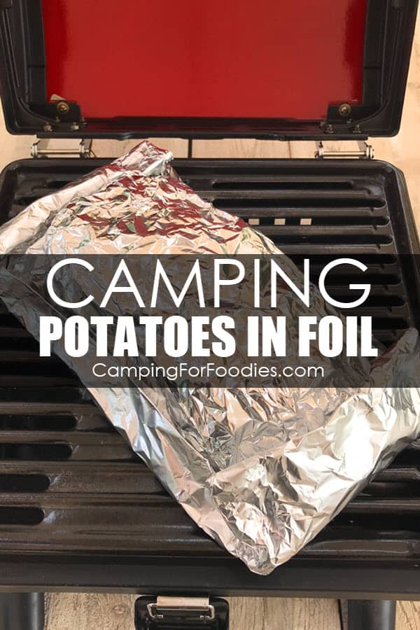 Grilled Camping Potatoes In Foil by CampingForFoodies features a folded and sealed tin foil packet that is ready to be cooked as it sits on a grill grate of a camping propane grill with text over the image that reads camping potatoes in foil.
