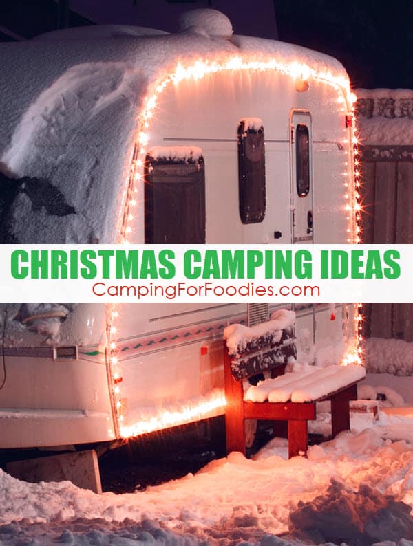 Christmas Camping Ideas by CampingForFoodies features a snow covered retro RV camper trailer with white Christmas lights around the entire side of the camper and a snow covered bench just outside the trailer door with text over the image reading Christmas camping ideas.