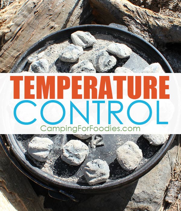 How To Maintain Dutch Oven Temperature Control When Camp Cooking by CampingForFoodies features a black cast iron camp Dutch oven sitting on the ground with charcoal briquettes on the lid and three firewood logs on the ground protecting the sides as a block from the wind with text over the image that reads temperature control.