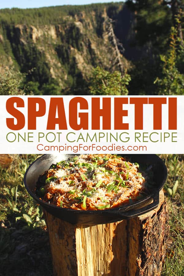 Spaghetti One Pot Camping Recipe by CampingForFoodies features a large black cast iron skillet setting on a tree stump against a background of beautiful rock formations and evergreen trees at a campsite, the pan is filled with pasta cooked in a sausage tomato sauce and topped with fresh basil and parmesan cheese with text over the image that reads spaghetti one pot camping recipe.