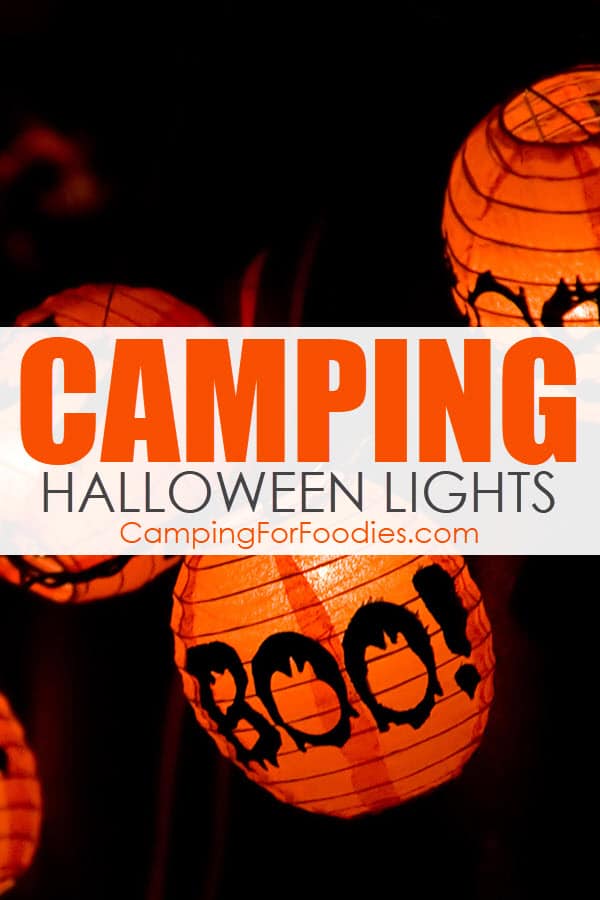 Halloween Camper Lights van CampingForFoodies heeft oranje en zwarte lampionnen met het woord BOO erop gedrukt terwijl ze tegen een donkere lucht hangen met tekst over de afbeelding die luidt camping Halloween lights.