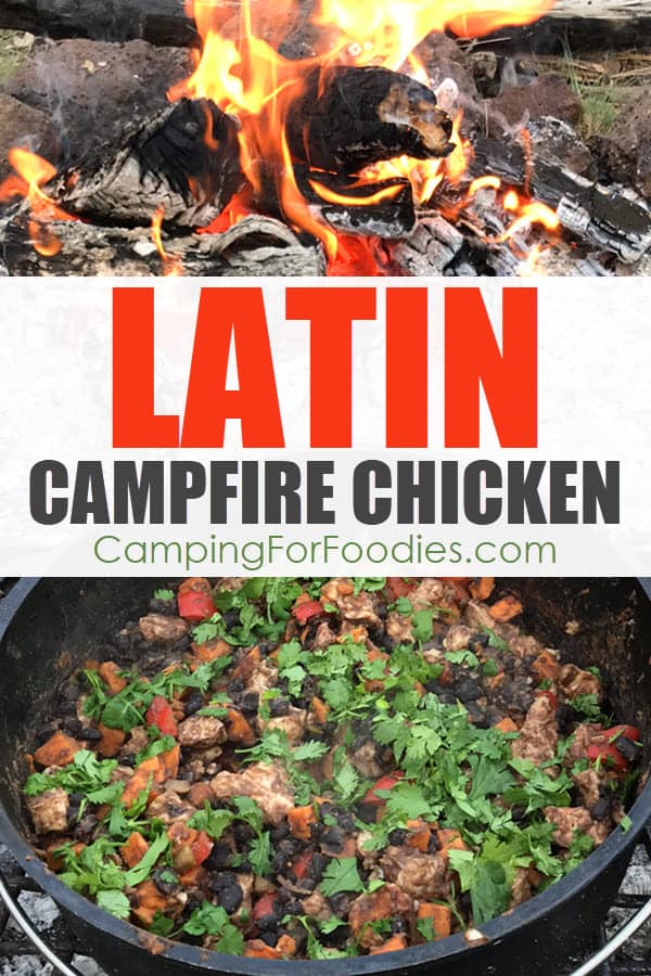 Latin Campfire Chicken by CampingForFoodies features a black cast iron camp Dutch oven in a campfire ring setting on a cooking grate filled with cooked chicken, sweet potatoes, red bell pepper, black beans and cilantro ready for serving at the campsite with a roaring campfire in the background with text over the image that reads Latin campfire chicken.