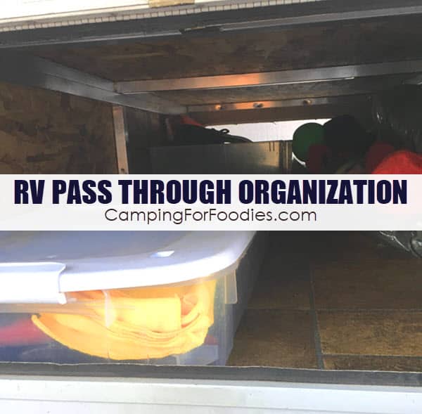 RV Pass Through Storage Organization by CampingForFoodies features an RV basement storage compartment with both side panels open and gear loaded on both sides including a storage box of tools, folded camp chairs and other camping items neatly organized for easy access with text over the image that reads RV pass through organization.