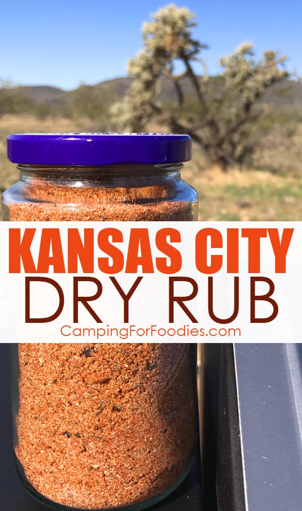 Barbecue Kansas City Dry Rub by CampingForFoodies features a glass jar filled with a red and brown colored mix of spices making a dry rub for smoking meats that is sitting on the top of a pellet box on a portable smoker with mountains and desert plants in the background at a campsite with text over the image that reads Kansas City Dry Rub.