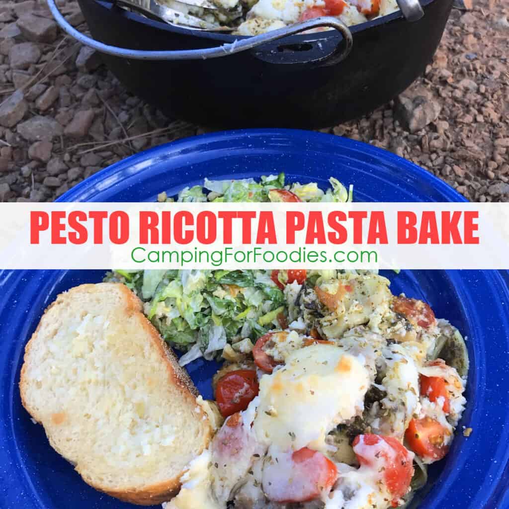 Baked Pesto Pasta With Ricotta by CampingForFoodies features a blue camping plate filled with a serving of this lazy man’s lasagna made with layers of Italian sausage, green basil pesto, cherry tomatoes, ricotta, mozzarella and parmesan cheese that is golden brown from baking. On the side is a tossed green salad and a thick slice of garlic bread. A black cast iron camp Dutch oven sits in the background that is filled with the remaining pesto pasta bake that is ready to be served with text over the image that reads Pesto Ricotta Pasta Bake.