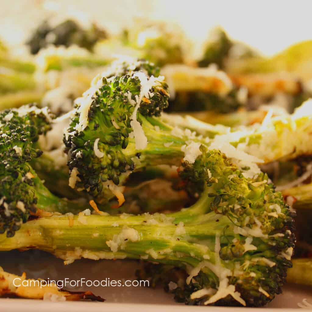 Burnt Broccoli Recipe by CampingForFoodies features a plate full of charred broccoli that is sprinkled with Parmesan cheese and ready to be served at the campsite.