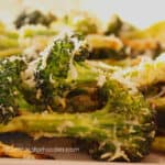 Burnt Broccoli Recipe by CampingForFoodies features a plate full of charred broccoli that is sprinkled with Parmesan cheese and ready to be served at the campsite.
