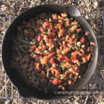 Smoked Green Beans by CampingForFoodies features a cast iron skillet filled with green beans, bacon, onions and garlic that have been smoked in a portable pellet grill and are ready to be served at the campsite.