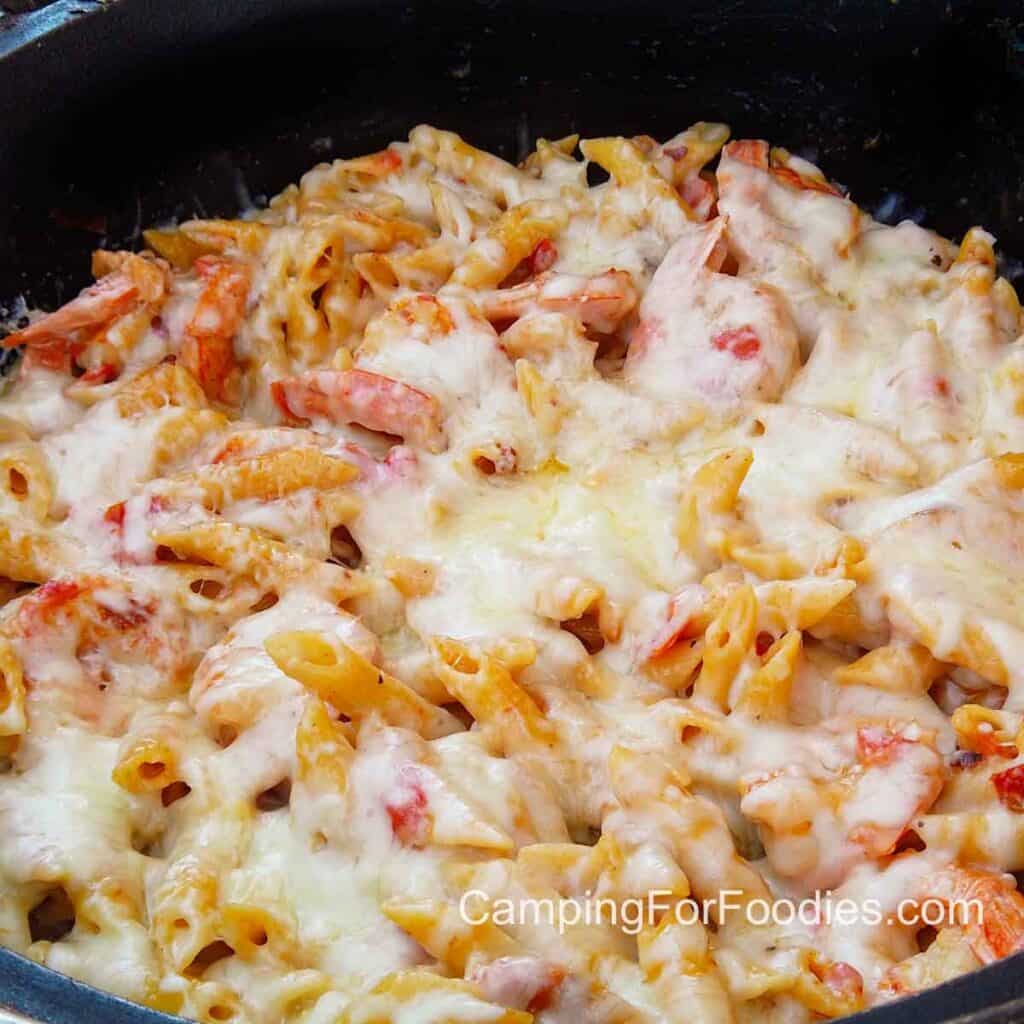 Dutch Oven Baked Shrimp Alfredo by CampingForFoodies features creamy garlicky shrimp alfredo baked in a black cast iron camp Dutch oven. The Shrimp and pasta one pot dinner is topped with melted mozzarella and parmesan cheese.