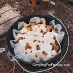 Dutch Oven Brownies by CampingForFoodies features a parchment-paper lined black cast iron camp Dutch oven filled with baked brownies, topped with golden-brown puffed mini marshmallows and graham cracker pieces.
