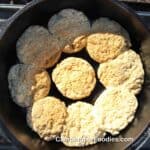 Dutch Oven Campfire Biscuits by CampingForFoodies features a black cast iron campfire Dutch oven filled with 9 freshly baked golden brown homemade biscuits.
