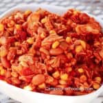 5 Can Camp Chili by CampingForFoodies features a white serving bowl filled with canned chicken meat that is covered in a red sauce from heating the meat with canned Mexican style corn, pinto beans, green chilies and salsa.