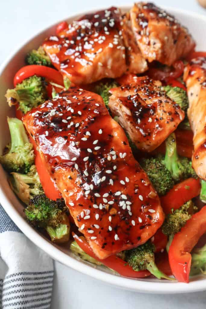 Salmon And Vegetables features a white bowl filled with glazed salmon over broccoli and red bell peppers.
