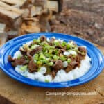 Asian Beef And Broccoli by CampingForFoodies features a blue camping plate filled with fluffy white rice topped with stir-fried beef strips and broccoli then topped with sliced green onions.