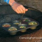 Run A Fork Around The Muffin Tin To Loosen Eggs by CampingForFoodies features a hand holding a fork along the inside of a muffin tin containing baked eggs topped with sliced green onions.