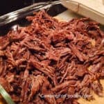 2-Ingredient Crockpot Shredded Beef Recipe by CampingForFoodies features a dish filled with shredded beef set on a wooden cutting board.