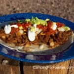 Shredded Beef Burritos by CampingForFoodies features a blue camping plate filled with a tortilla topped with shredded beef, shredded cheese, onions, salsa, cubed avocado and drizzled with sour cream.